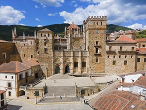 Aerial view of the facade of a monastery with red roofs and wide stairs under a blue sky in Spain.