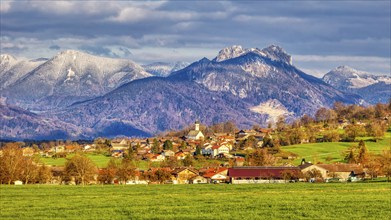 Idyllic village in front of an alpine mountain landscape with snow-covered peaks and green meadows