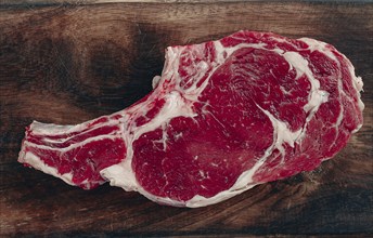 Raw rib eye steak, cowboy steak, wooden chopping board, marble table, top view, no people