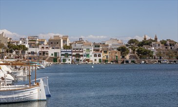 Quiet harbour with boats in the foreground and colourful buildings along the coast under a blue