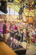 Band plays on a stage in a colourful marquee in front of a large crowd, Canstatter Wasen,