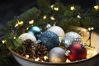 Christmas tree ornaments in a bowl, featuring a mix of glass baubles, pine cones, and fairy lights,