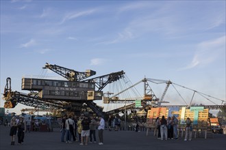 Festival visitors in front of open-cast mining excavator and Melt logo at the Melt Festival in