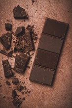 Chocolate bar, for the manufacture of confectionery, broken, crumbled, on a brown background, top