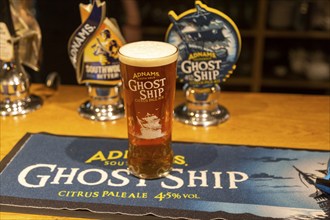 Pint glass of Adnams Ghost Ship Citrus pale Ale, on beer mat with bar pumps, Suffolk, UK