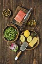 An assortment of fresh ingredients on a wooden surface, including salmon fillet, avocado, lemon,