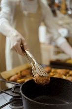 Closeup view of transferring meat patties from a baking tray to a saucepan using kitchen tongs