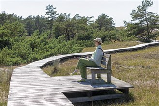 Elderly, woman sitting on bench, wooden footbridge, reed grass, trees, circular hiking trail,