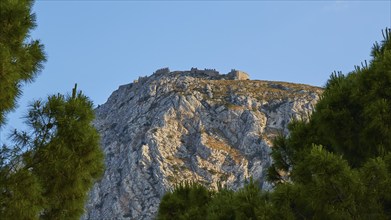 An ancient castle crowning a majestic hilltop, framed by fir trees, Archaic Castle, Akrokorinthos,