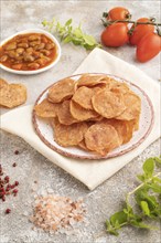 Slices of dehydrated salted meat chips with herbs and spices on gray concrete background and white