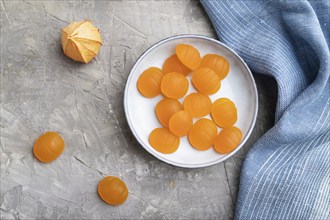 Jelly pumpkin candies on gray concrete background and blue linen textile. close up, top view, flat