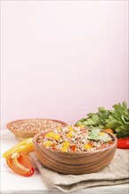 Buckwheat porridge with vegetables in wooden bowl on a pink background and linen textile. Side