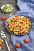 Tortiglioni semolina pasta with tomato and microgreen sprouts on a black concrete background and