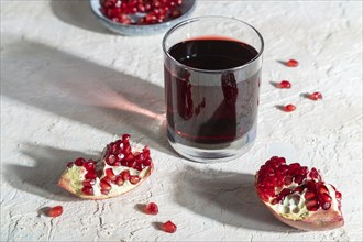 Glass of pomegranate juice on a white concrete background. Hard light, contrast. Side view, close