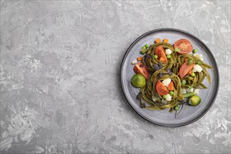 Tagliatelle green spinach pasta with tomato, pea and microgreen sprouts on a gray concrete