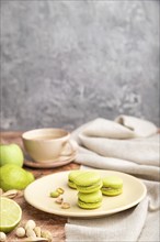 Green macarons or macaroons cakes with cup of coffee on a brown and gray concrete background and