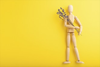 Wooden mannequin holding lavender flowers on yellow pastel background. copy space, isolated,