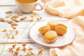 Orange macarons or macaroons cakes with cup of apricot juice on a white wooden background and