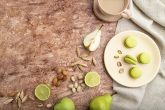 Green macarons or macaroons cakes with cup of coffee on a brown concrete background and linen