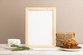 White wooden frame mockup with cup of coffee and cake on brown background. Blank, side view, still