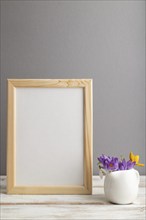 Beige wooden frame mockup with snowdrop crocus flowers on gray paper background. Blank, vertical