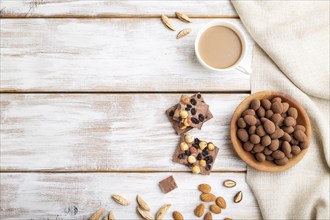 Almond in chocolate dragees in wooden plate and a cup of coffee on white wooden background and