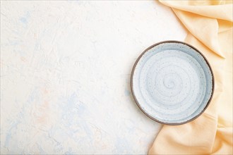 Empty blue ceramic plate on white concrete background and orange linen textile. Top view, copy