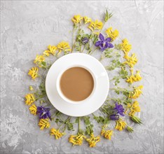 Yellow and blue flowers in a spiral and a cup of coffee on a gray concrete background. Morninig,