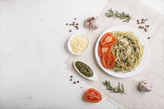 Spaghetti pasta with pesto sauce, tomatoes and cheese on a linen tablecloth on white wooden