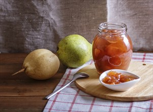 Pear jam in a glass jar on a linen tablecloth on a wooden table. Homemade, copy space