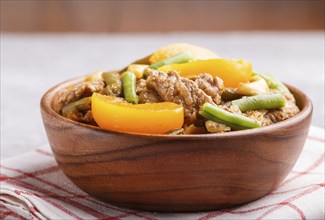 Fried pork with peaches, cashew and green beans in a wooden bowl on a gray concrete background.