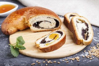 Homemade yeast rolls with poppy seeds and honey on a wooden kitchen board on a black concrete