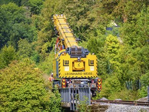 Yellow crane from Leonhard Weiss on a railway line working in a wooded area, track construction,