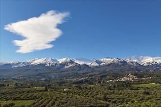 Snow-capped mountains under blue sky and clouds with green valley and village in the foreground,