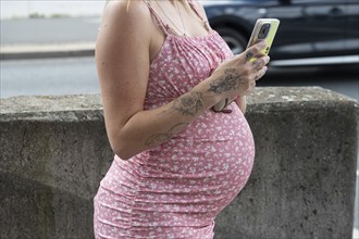 Belly of a young pregnant woman with mobile phone, Bavaria, Germany, Europe