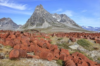 Rusted oil barrels on a fjord in front of steep mountains, remains of a US airbase from the Second