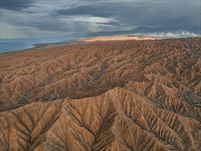 Landscape of eroded hills, badlands at sunset, Issyk Kul Lake in the background, aerial view,