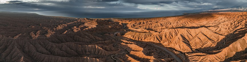 Panorama, landscape of eroded hills, badlands at sunset, Issyk Kul Lake in the background, aerial