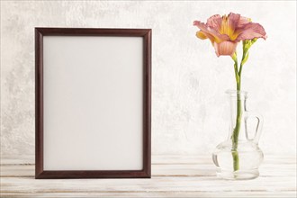 Wooden frame with purple day-lily flowers in glass vase on gray concrete background. side view,