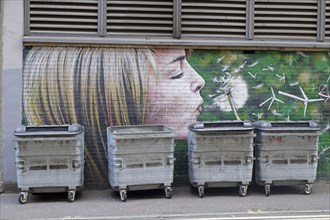 A mural shows a girl blowing a dandelion in front of rubbish containers, Mural Trail, Glasgow,