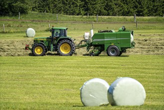 Hay harvest, farmer with agricultural machine, picks up mown hay, which is immediately pressed into