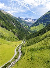 A wide valley with a meandering river, surrounded by green meadows and wooded mountains under a