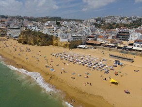 Lively sandy beach with many bathers and urban surroundings in the background, aerial view,