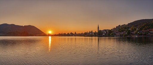 A warm, peaceful sunset picture with a lake, surrounding mountains and a village, Schliersee