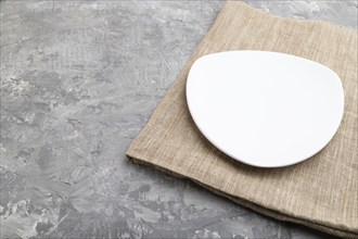 Empty white plate on gray concrete background and linen textile. Side view, copy space