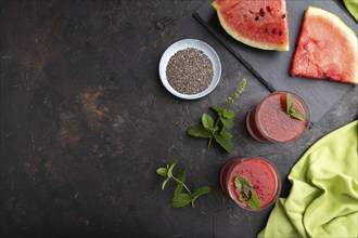 Watermelon juice with chia seeds and mint in glass on a black concrete background with green