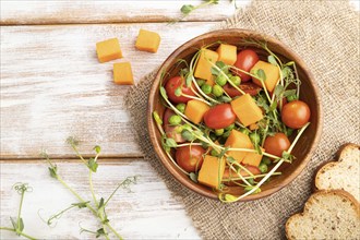 Vegetarian vegetable salad of tomatoes, pumpkin, microgreen pea sprouts on white wooden background