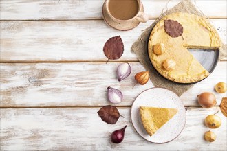 Autumn onion pie decorated with leaves and cup of coffee on white wooden background and linen