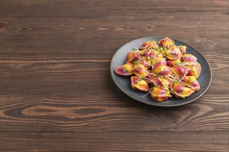 Rainbow colored dumplings with pepper, herbs, microgreen on brown wooden background. Side view,