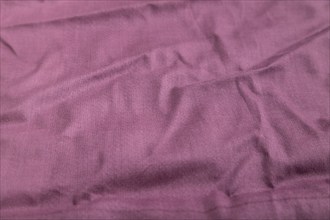 Fragment of smooth cotton purple tissue. Side view, natural textile background and texture